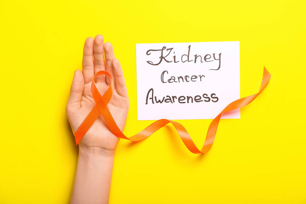 Paperilevy, jossa teksti KIDNEY CANCER TIETOISUUS, naisten käsi ja oranssi nauha keltaisella pohjalla - Valokuva, kuva