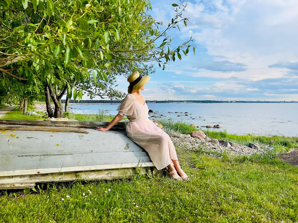  donna siede su una vecchia barca di legno in un bosco campo selvaggio e guarda il mare all'orizzonte - Foto, immagini