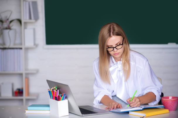 Female college student preparing for test or exam, writing, using computer laptop in classroom - Φωτογραφία, εικόνα