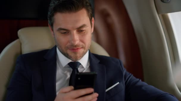 Úspěšný muž hledící na chytrý telefon v okně letadla. Nadšený obchodník odpočívá a kontroluje sociální sítě, čte si zprávy na služební cestě v obleku. Jistý finanční analytik těší rolování mobilní telefon - Záběry, video
