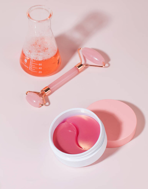 Hydrogel pink patches, quartz roller and laboratory flask on a pink background. Anti-aging facial skin care. - Foto, Imagem
