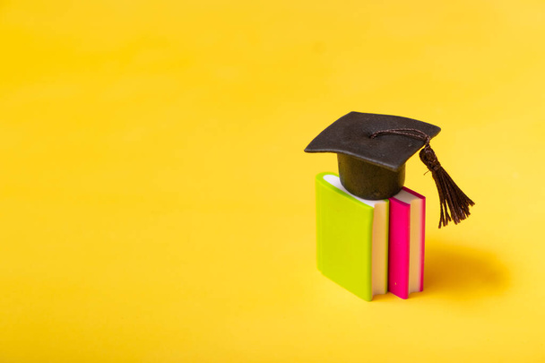 Καπέλο αποφοίτησης σε πολύχρωμα βιβλία σε κίτρινο φόντο. Εκπαίδευση έννοια με αντίγραφο χώρο. - Φωτογραφία, εικόνα