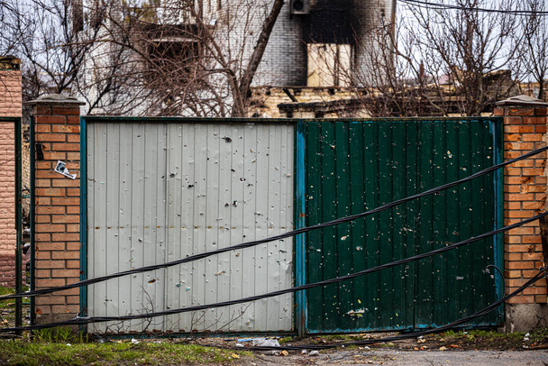 Irpin, Region Kyev Ukraine - 09.04.2022: Von russischen Soldaten beschossene Tore, Besatzer. Die Tore, der Zaun, das Haus wurden aus einem Maschinengewehr geschossen, einem Maschinengewehr.. - Foto, Bild