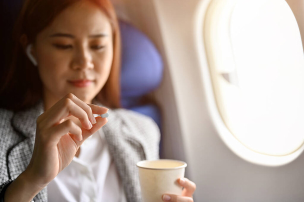 Jonge Aziatische vrouwelijke passagier voelt zich duizelig, het nemen van een luchtziekte ziekte ziekte pillen voordat u opstijgen op haar stoel. Vervoers- en gezondheidsconcept - Foto, afbeelding