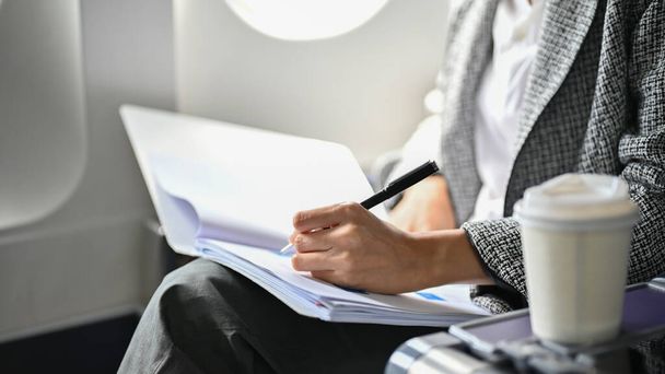 обрезанный имидж, профессиональная и успешная деловая женщина пишет что-то на своем бизнес-документе, удаленно работает на самолете. - Фото, изображение