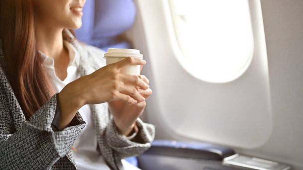 Abgeschnittenes Bild, eine erfolgreiche asiatische Geschäftsfrau nippt während des Fluges an einem heißen Kaffee oder Tee. - Foto, Bild