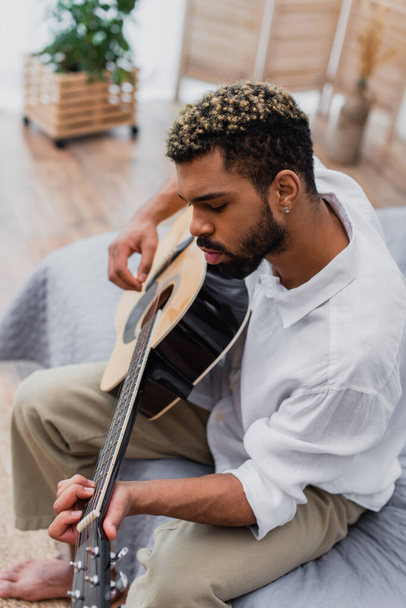 high angle view of african american man with dyed hair playing acoustic guitar at home - Foto, imagen