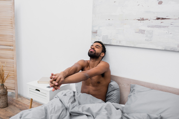 shirtloze Afro-Amerikaanse man met gebalde handen stretching in bed - Foto, afbeelding