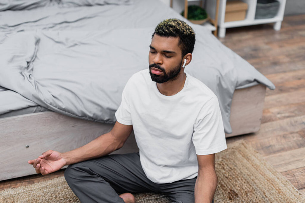 Sakallı, Afro-Amerikan bir adamın evde yatarken gözleri kapalı meditasyon yapmasının yüksek açılı görüntüsü. - Fotoğraf, Görsel