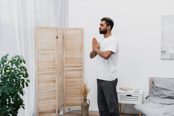 bearded african american man meditating with praying hands near folding screen - Photo, Image
