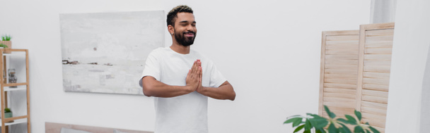 glücklich afrikanisch-amerikanischer Mann afrikanisch-amerikanischer Mann meditiert mit betenden Händen in der Nähe von Klappbildschirm, Banner - Foto, Bild
