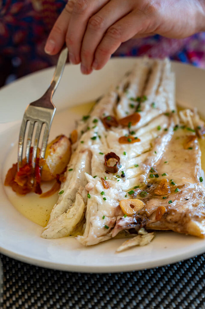 Eten in restaurant van vers gegrild met knoflook en olijfolie op oude houtskool parrilla 's witte zeebaars vis in klein vissersdorpje Getaria, Baskenland, Spanje - Foto, afbeelding
