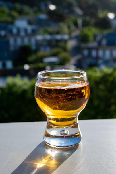 Одна склянка яблучного сидру п "є в сонячних променях і будинках села Етрета на задньому плані (Нормандія, Франція). - Фото, зображення