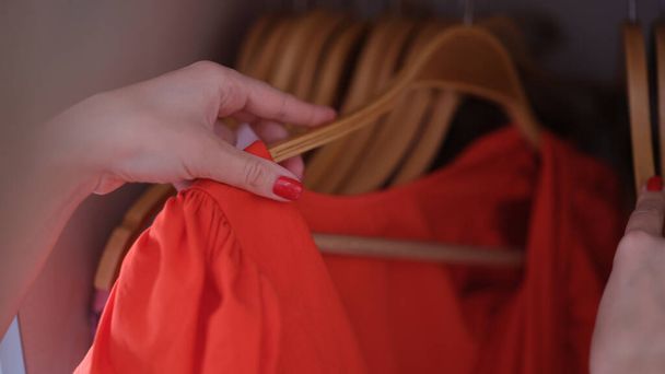 Vrouwelijke hand kiezen rode jurk op hanger kast closeup. Bijzonder gelegenheidskleding concept - Foto, afbeelding