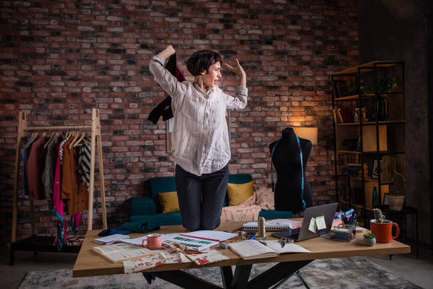 Happy and crazy fashion designer lady dancing with a red dress over the work table and enjoy the time at work in her tailoring atelier. - 写真・画像