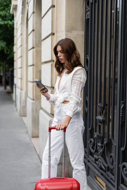 Trendi nő bőrönddel mobiltelefont használ a városi utcában Párizsban  - Fotó, kép