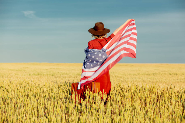Girl in USA flag with suitcase in wheat field with blue sky on background - Photo, Image