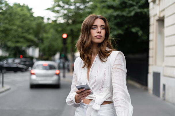 Brunette traveler in blouse holding smartphone near road in Paris  - Foto, Imagem