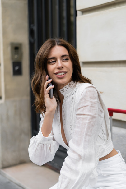 Smiling tourist talking on cellphone near blurred building on street in Paris  - Φωτογραφία, εικόνα