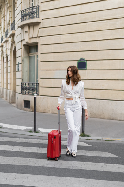 Fashionable traveler with suitcase walking on crosswalk on street in Paris  - Fotografie, Obrázek
