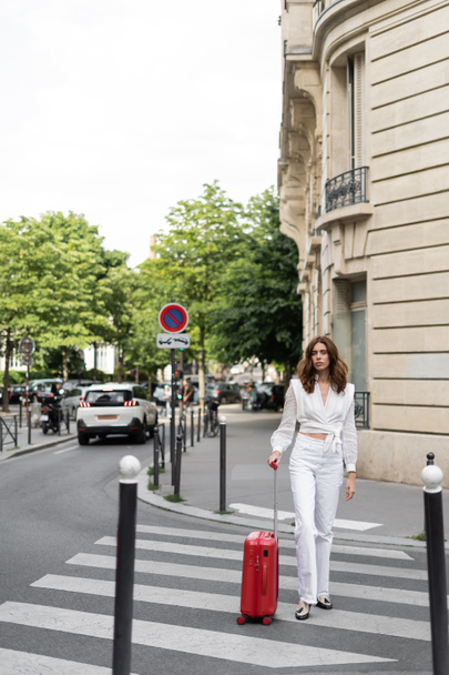 Brunette traveler with baggage walking on crosswalks on street in France - Photo, Image