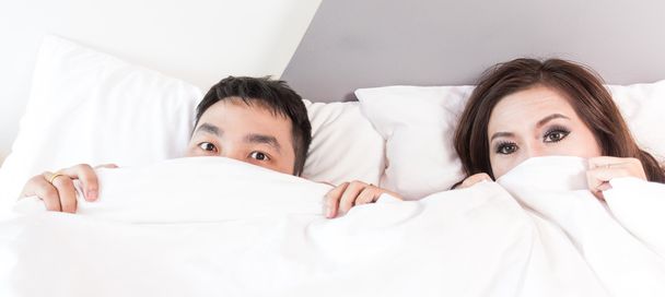 Funny couple in bed looking and peeking over sheets surprised - Foto, Imagen
