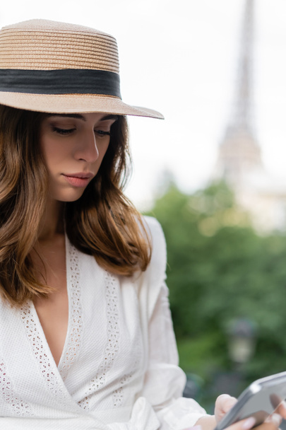 Stylische Frau mit Sonnenhut mit Smartphone im Freien in Paris  - Foto, Bild