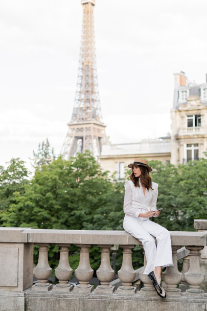 パリを背景にエッフェル塔のある通りにスマートフォンを保持するトレンディな旅行者  - 写真・画像