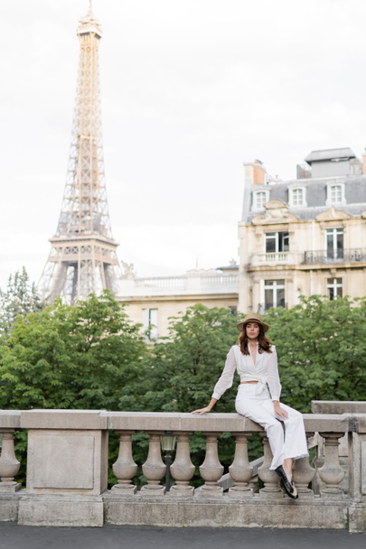 Цікава жінка тримає смартфон і дивиться на камеру на вулиці з Ейфелевою вежею на задньому плані в Парижі.  - Фото, зображення