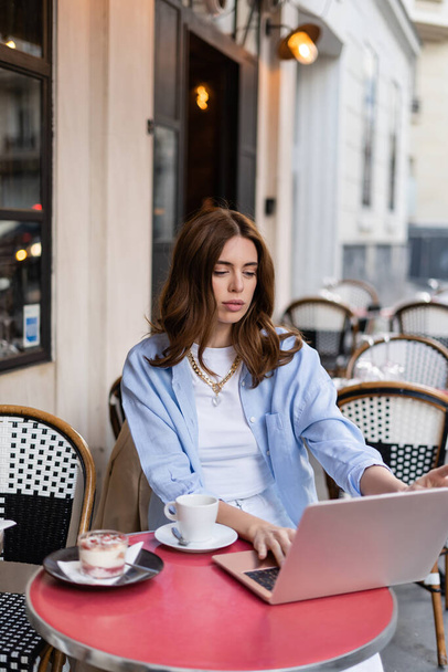 Trendy freelancer using laptop near coffee and dessert in outdoor cafe in Paris  - Фото, изображение