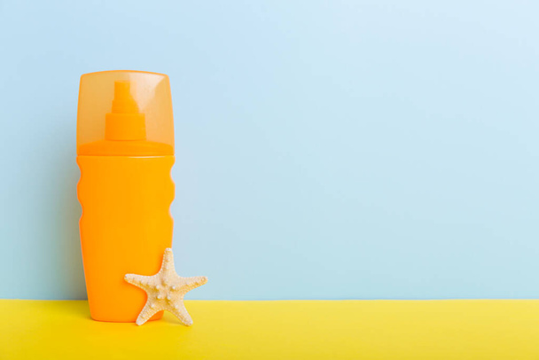 Beach accessories. Moisturiser sunscreen suntan lotion bottle for UVB skincare protection in summer with seashells on colored background. Mock up with copy space. - Foto, Imagem