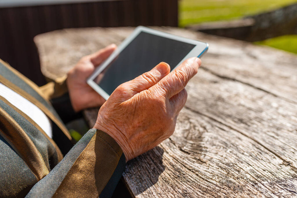 Hands of senior woman holding tablet PC, szabadban, meleg nyári nap.Close up.Selective focus. - Fotó, kép