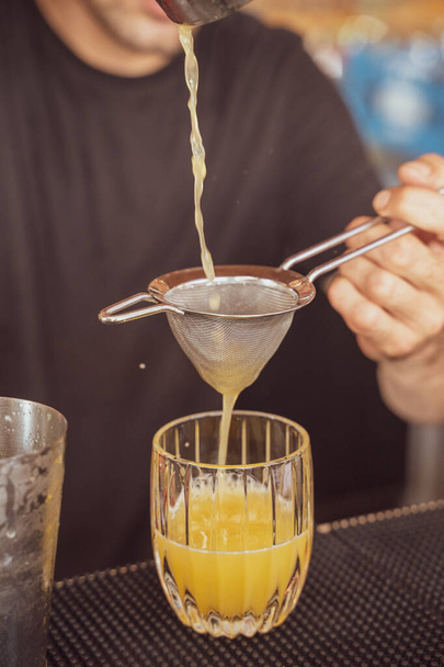 Een verticaal shot van een barman bereidend ijsje verfrissende gele cocktail in een pub - Foto, afbeelding