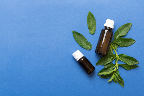 Natural Mint Essential Oil in a Glass Bottle. organic cosmetics with herbal extracts of mint on colored background. - Фото, изображение