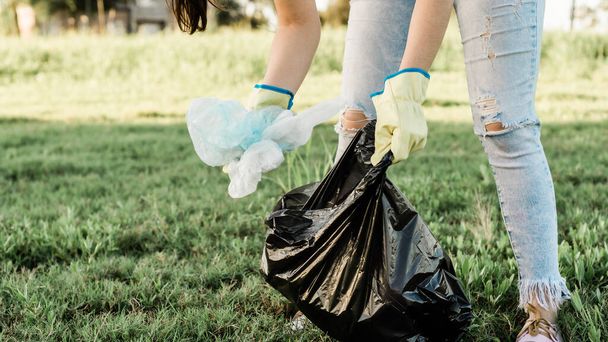 Person caring for our planet earth by collecting garbage from the ecosystem, dressed in jeans, a white shirt and yellow gloves. - Photo, Image