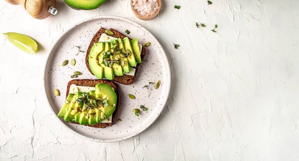 Healthy avocado toasts with rye bread, sliced avocado, cheese, pumpkin, nut and sesame for breakfast or lunch. Vegetarian food. Vegan menu. Food recipe background. Close up. - 写真・画像