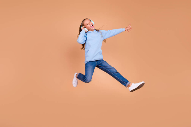 Full body portrait of overjoyed carefree person jump arm touch headphones isolated on beige color background. - Foto, immagini