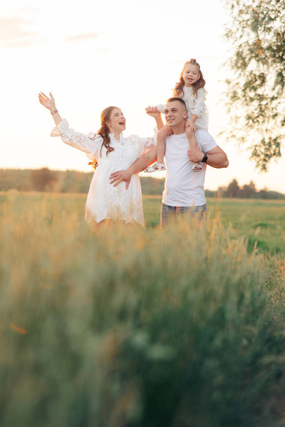 Happy family walks on meadow and father carries daughter on his shoulders during outing. - Zdjęcie, obraz