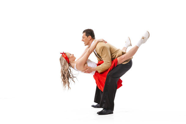 Live and emotions. Excited young couple of dancers in vintage retro style outfits dancing social dance isolated on white background. Timeless traditions, 60s ,70s american fashion style. - Photo, Image