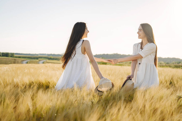 Two pretty sisters in a field of wheat. Beautiful two girls with long healthy hair enjoying nature on summer. - Foto, afbeelding