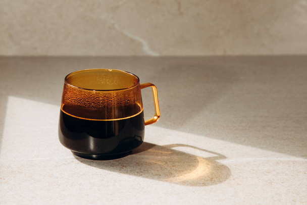 Черный кофе в прозрачной оранжевой чашке на бежевом светлом фоне. Вид спереди - Фото, изображение