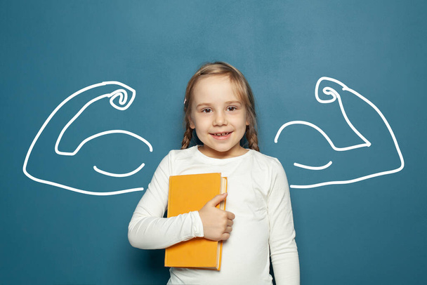 Счастливая маленькая девочка с книгой и мускулами на синем фоне. Власть в образовании - Фото, изображение