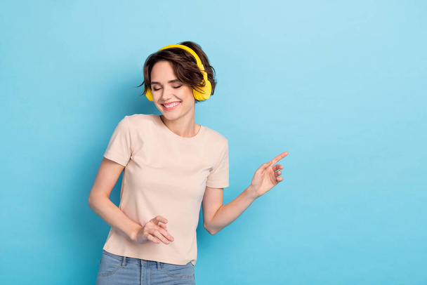 Photo of cute adorable lady dressed beige t-shirt earphones listening songs empty space isolated blue color background. - 写真・画像