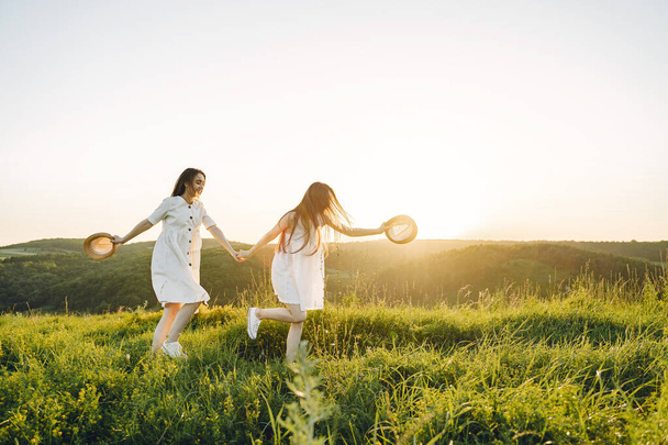 Δύο όμορφες αδερφές σε ένα χωράφι με σιτάρι. Όμορφα δύο κορίτσια με μακριά υγιή μαλλιά απολαμβάνοντας τη φύση το καλοκαίρι. - Φωτογραφία, εικόνα