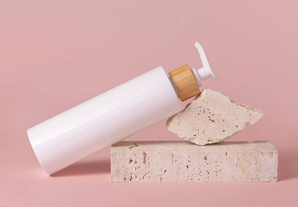 White one pump bottle lies on travertine stone on light pink, close up, mockup. Skincare beauty product. Natural cosmetics, lotion or cleanser. Minimal compositio - Photo, Image
