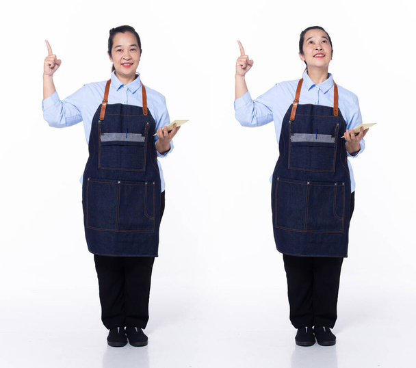 Pełna długość lat 40-tych Azjatka Seniorek kelnerka baristka kawy, wskazując palcem w powietrzu, nosić białe formalne spodnie mundurowe. Uśmiech cafe kobieta stoi uśmiech szczęśliwy na białym tle odizolowany - Zdjęcie, obraz