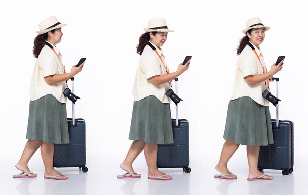 Plná délka 40s 50s Asijské Senior Woman dovolená turista, kráčející vpřed vlevo vpravo, nosit tropické šaty pantofle. Úsměv žena nést mapu internet telefon zavazadla přes bílé pozadí izolované - Fotografie, Obrázek