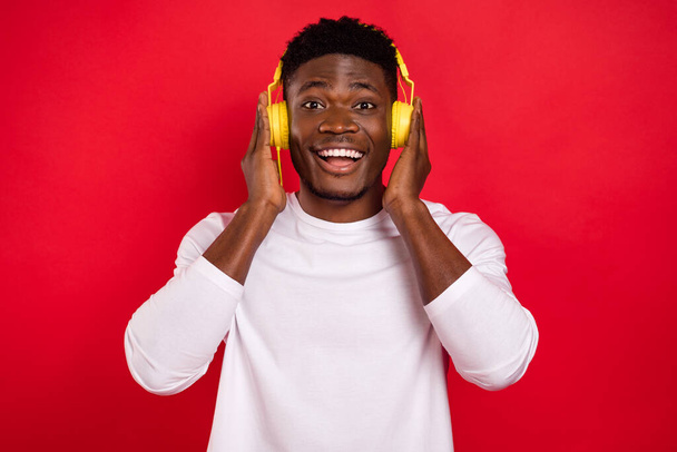Photo of astonished cheerful person hands touch headphones isolated on red color background. - Foto, Imagem