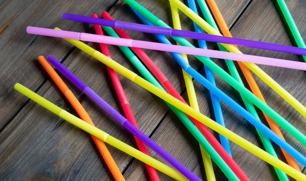 Many colored cocktail straws are scattered across the wooden table. On a wooden background are plastic straws for drinks. Straws for drinks. Ecological straws. - Foto, Bild