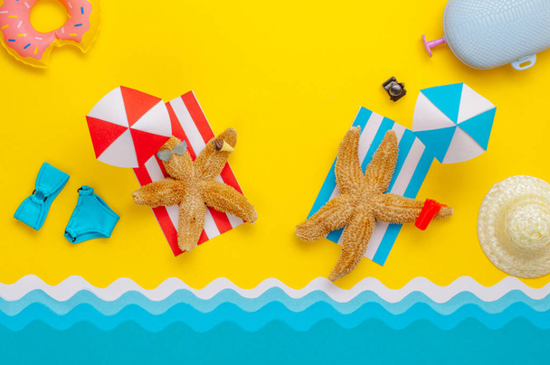 Seesterne ruhen am Strand in der Nähe von Papierschirmen mit Spielzeuggetränk und Sonnenbrillen. Sommerurlaub minimalistisches, kreatives Gestaltungskonzept. Papierkunst Hintergrund mit Leerraum für Text. - Foto, Bild